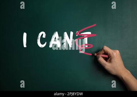 Woman crossed out letter T in phrase I CAN'T written on green chalkboard, closeup. Motivation and positivity Stock Photo