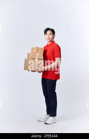 young man in red shirt carrying three carton boxes on a white wall Stock Photo