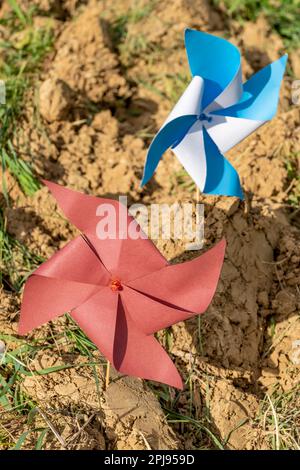 Two pinwheels, one red and the other white and blue, are stuck in clods of freshly plowed earth Stock Photo