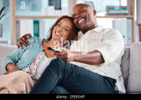 Couple, watching tv and smile on sofa in home living room, bonding and cuddle. Interracial, television and happiness of black man and mature woman Stock Photo
