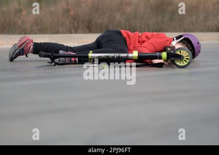 Little girl's tumble: scooter accident on pavement. Stock Photo