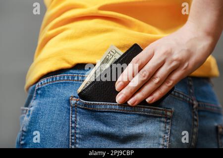 A woman's hand take out a black leather wallet with American dollars from the back pocket of her jeans. Close-up, back view. The concept of salary, sa Stock Photo