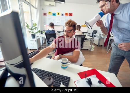 A manager is yelling on a sleepy employee through a megaphone at work in a uniform atmosphere in the office. Employees, job, office Stock Photo