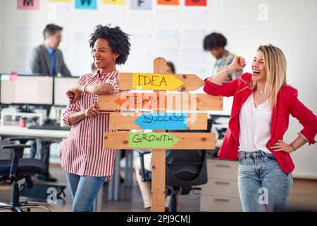 Two young cheerful female office worker are promoting company slogans while posing for a photo in a pleasant atmosphere in the office. Employees, job, Stock Photo