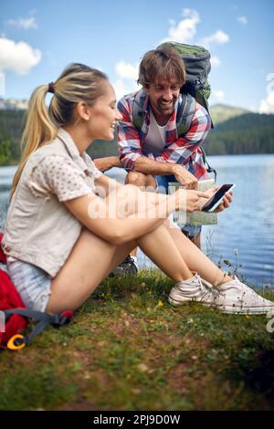 Couple on hike. Woman sitting in grass showing to mobile. Hiking, lifestyle, nature concept Stock Photo