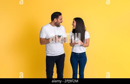 Excited young adult couple in white t-shirts looking at each other and screaming cheerfully winning and celebrating while using smart phones isolated Stock Photo