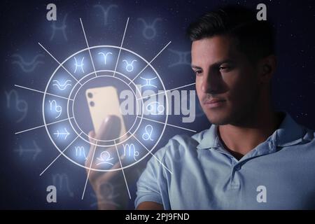 Man with smartphone reading daily horoscope on dark background Stock Photo