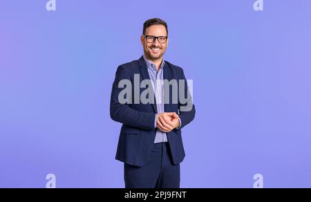 Smiling elegant mid adult male manager dressed in blue suit clasping his hands while standing confidently isolated over blue background Stock Photo