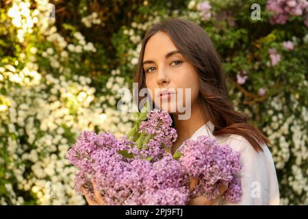 Attractive young woman with lilac flowers outdoors Stock Photo