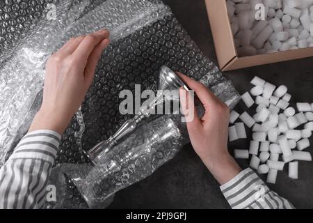 Woman covering silver candlesticks with bubble wrap at dark grey table, closeup Stock Photo