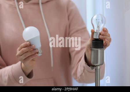 Woman changing incandescent light bulb for fluorescent one in lamp at home, closeup. Saving energy concept Stock Photo