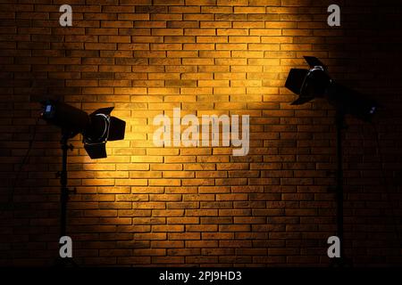 Bright yellow spotlights near brick wall in dark room, space for text Stock Photo