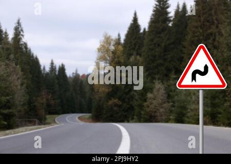 Traffic sign DOUBLE BEND FIRST TO RIGHT near empty asphalt road going through coniferous forest Stock Photo