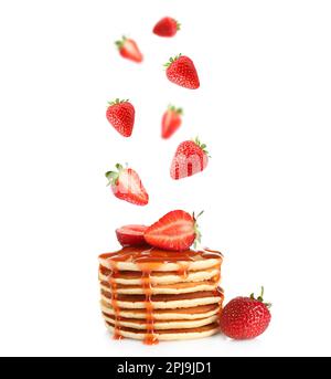 Fresh strawberries falling onto stacked pancakes against white background Stock Photo
