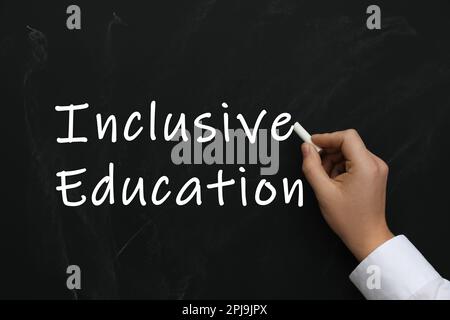 Woman writing phrase INCLUSIVE EDUCATION on blackboard, closeup Stock Photo