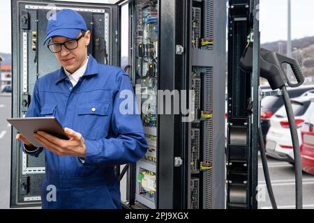 Serviceman with digital tablet repairing charging station for electric vehicles. High quality photo Stock Photo