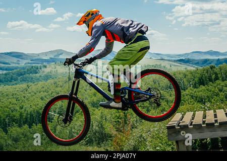 male rider on downhill bike jumping wooden drop, racing DH mountain bike, extreme sport games Stock Photo
