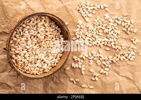 Organic pearl barley in coconut shells on kraft paper, close-up, top view. Stock Photo
