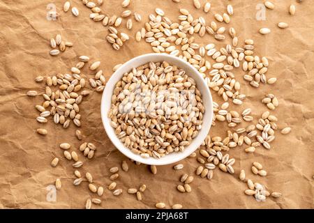 Organic pearl barley in white saucer on kraft paper, close-up, top view. Stock Photo