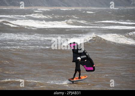 A Wing foil surfer skims through a choppy sea powered by a stiff breeze off the Jurrasic coast in Lyme Bay. Dorset.UK Stock Photo