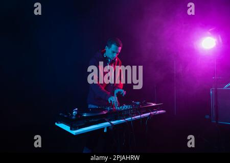 Professional DJ mixing vinyl records on a hip hop party. White male person playing music set in night club Stock Photo