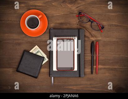 Top view of notepad, cellphone, purse with  money and coffee cup on wooden table Stock Photo