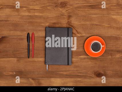 Black diary, pens and cup of coffee on wooden table Stock Photo