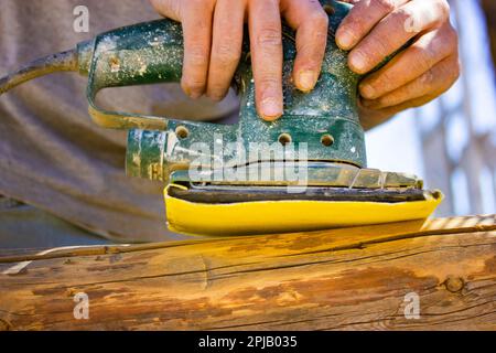 Craftsman's hands close up with old polishing machine on wooden logs. Working on wood with a special woodworking machine. Carpenter or engineer master Stock Photo