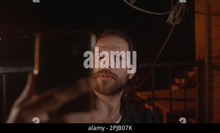 Young Man Video Calling on a House Balcony at Night, Surprised Guy Talking on Phone in Late Evening House Balcony Stock Photo