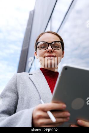 Female entrepreneur wearing glasses holding digital tablet in hands. Stock Photo