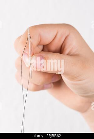 Detail of hand holding needle with thread on white background Stock Photo