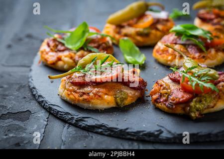 Homemade small pizza with pesto, salami, tomatoes and arugula on black background Stock Photo