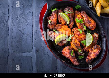 Roasted chicken wings in barbecue sauce with lime and baked potatoes in rustic pan Stock Photo