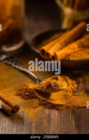Cinnamon powder in vintage spoon with cinnamon sticks on wooden background as cooking and baking ingredient Stock Photo