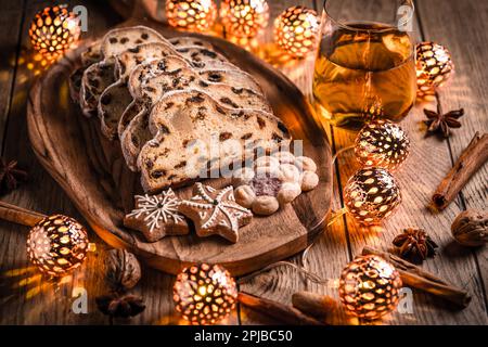 Christmas Stollen and cookies with apple mulled wine and Christmas lights. Traditional Sweet Fruit Loaf with icing sugar Stock Photo