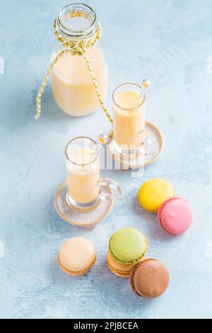Assorted delicious French macarons with egg liqueur or eggnog on blue background Stock Photo