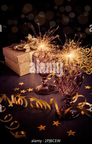 New Years Eve home setting table with sparklers in wine glass with gift box and carnival mask Stock Photo