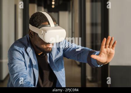 Man in vr headset exploring metaverse world, touching virtual reality subjects. Abstract cyber world in office Stock Photo