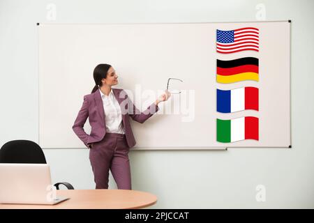 Foreign languages teacher near whiteboard with different flags in modern classroom Stock Photo