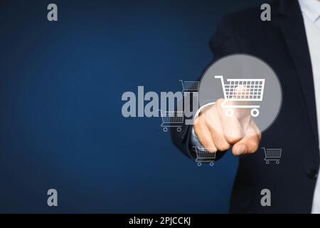 Man demonstrating virtual image of shopping cart on dark blue background, closeup. Space for text Stock Photo