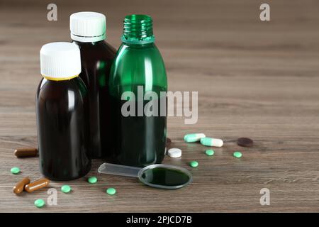 Bottles of cough syrup, dosing spoon and pills on wooden table Stock Photo