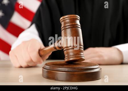 Judge with gavel at light wooden table near American flag, closeup Stock Photo