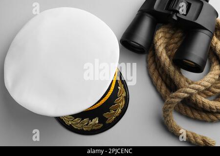 Peaked cap, rope and binoculars on light grey background, flat lay Stock Photo