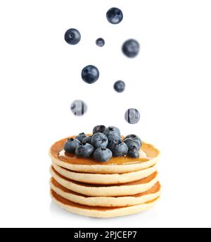 Fresh blueberries falling onto stacked pancakes against white background Stock Photo