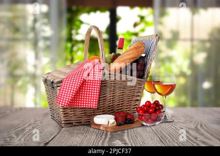 Wicker picnic basket with wine and different products on wooden table indoors Stock Photo