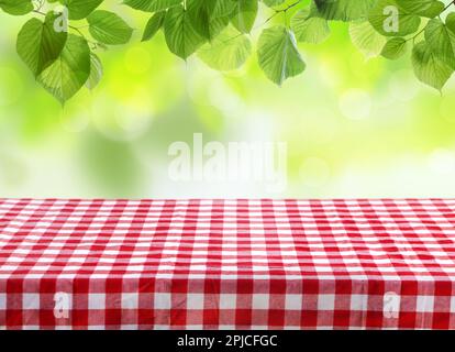 Table with checkered picnic cloth outdoors on sunny day. Space for design Stock Photo