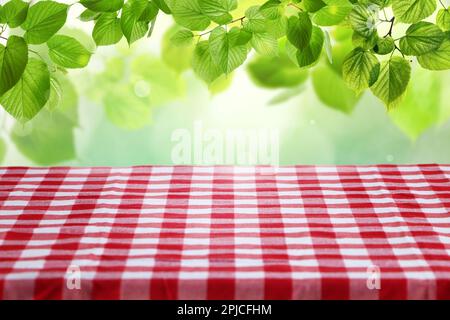 Table with checkered picnic cloth outdoors on sunny day. Space for design Stock Photo