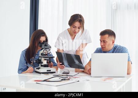 Using microscope. Group of young doctors is working together in the modern office Stock Photo