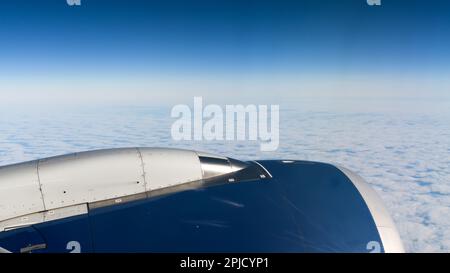 View over a blue aircraft engine at high altitude above white clouds with horizon Stock Photo