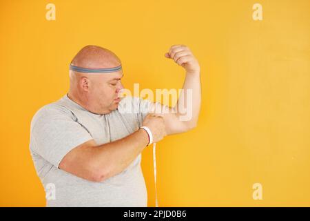 Funny overweight man in sportive head tie is against yellow background Stock Photo